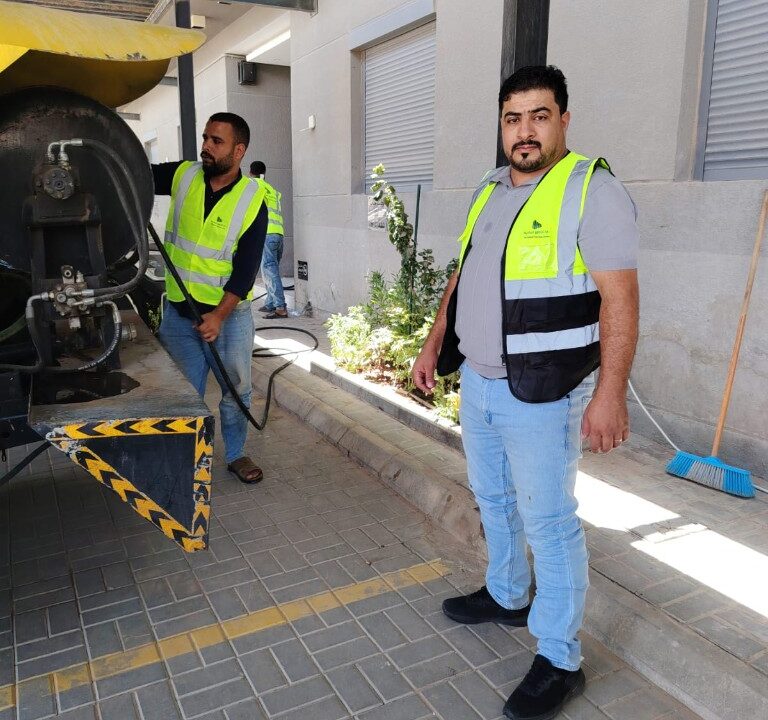 فنيو دارة التطوير العقارية أثناء الصيانة الدورية باستخدام معدات شفط وضغط بجانب مبنى سكني في الرياض