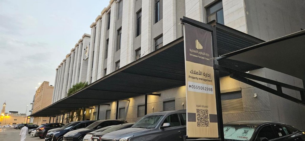 إدارة أملاك عقارية على ثلاث واجهات: اللافتة والمقر والممر بنر دارة التطوير لإدارة الأملاك أمام مبنى ومظلة مواقف في الرياض